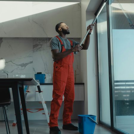 A man in coveralls cleans a large window in a stylish, modern home interior.