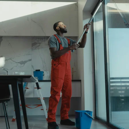 A man in coveralls cleans a large window in a stylish, modern home interior.